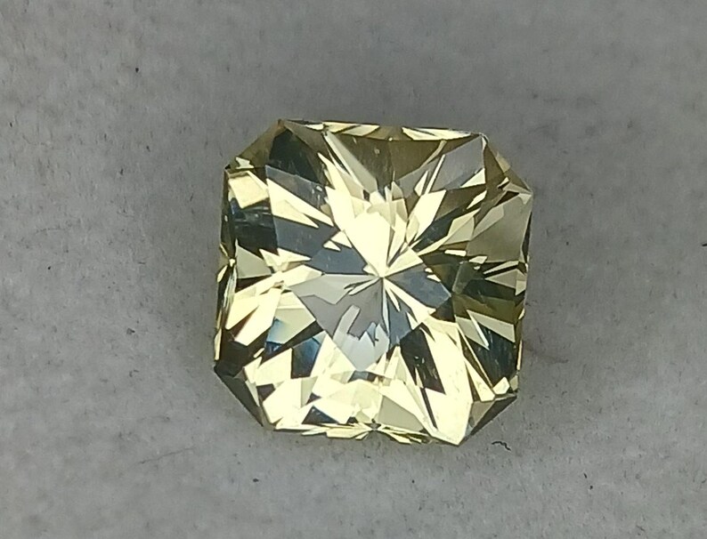 May include: A light yellow gemstone with a square shape and a faceted cut.