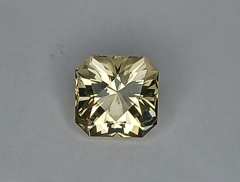 May include: A light yellow, faceted gemstone with a square shape.