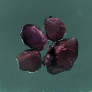 May include: Four small, dark purple gemstones, possibly rubies, on a green surface.