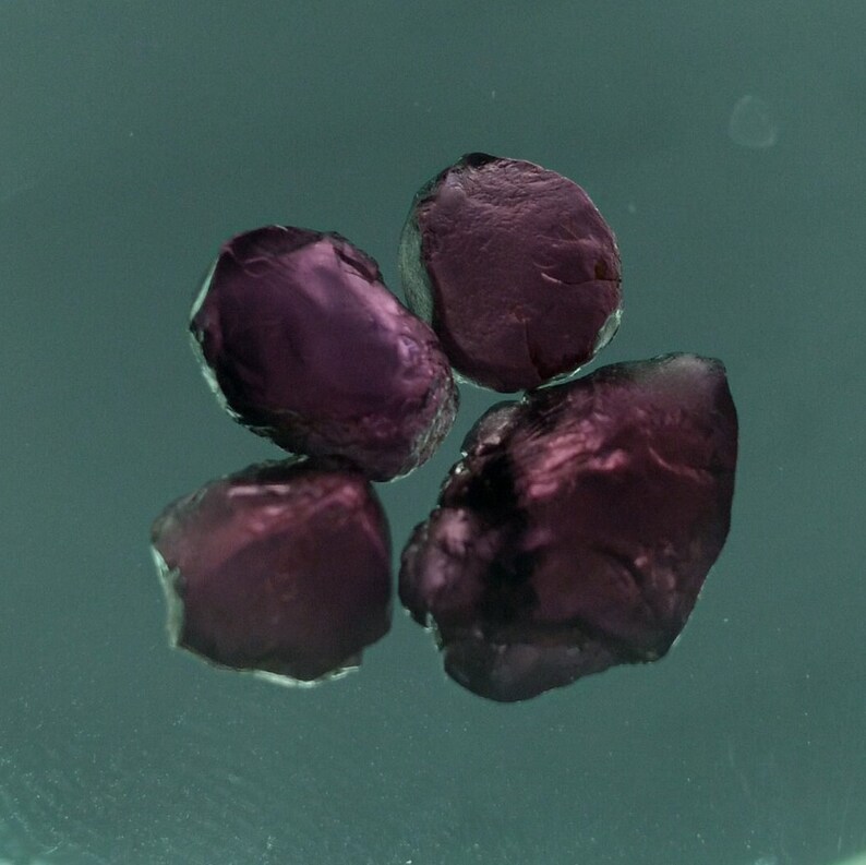 May include: Four small, dark purple gemstones, possibly rubies, on a green surface.