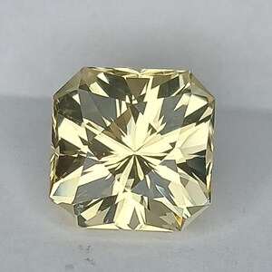 May include: A yellow gemstone with a square shape and a faceted cut. The gemstone has a star-like pattern in the centre.