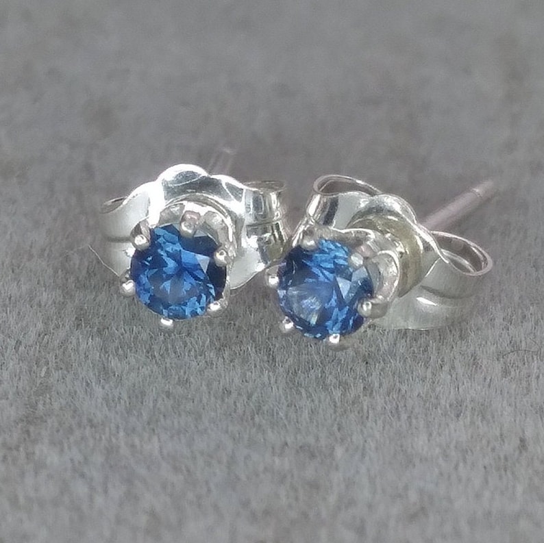 Puede incluir: Un par de pendientes de plata con una piedra preciosa azul en cada uno. Los pendientes tienen un dise&ntilde;o simple y elegante.