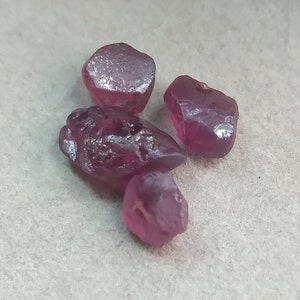 May include: Four rough, dark pink gemstones. The gemstones are irregularly shaped and have a translucent appearance.
