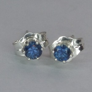 Puede incluir: Un par de pendientes de plata con detalles de piedras preciosas azules. Los pendientes tienen un dise&ntilde;o &uacute;nico y ondulado.