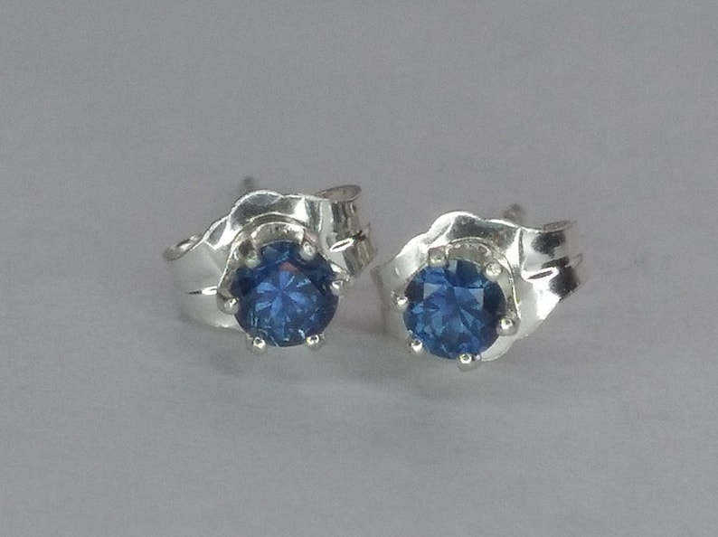 Puede incluir: Un par de pendientes de plata con detalles de piedras preciosas azules. Los pendientes tienen un dise&ntilde;o &uacute;nico y ondulado.