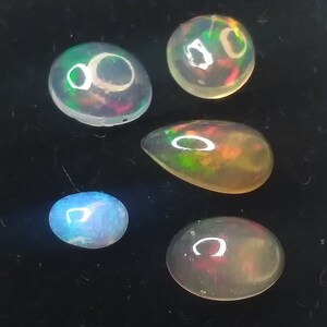 May include: Five opal gemstones of various shapes and sizes, including round, oval, and teardrop, with iridescent colors of green, blue, and red.
