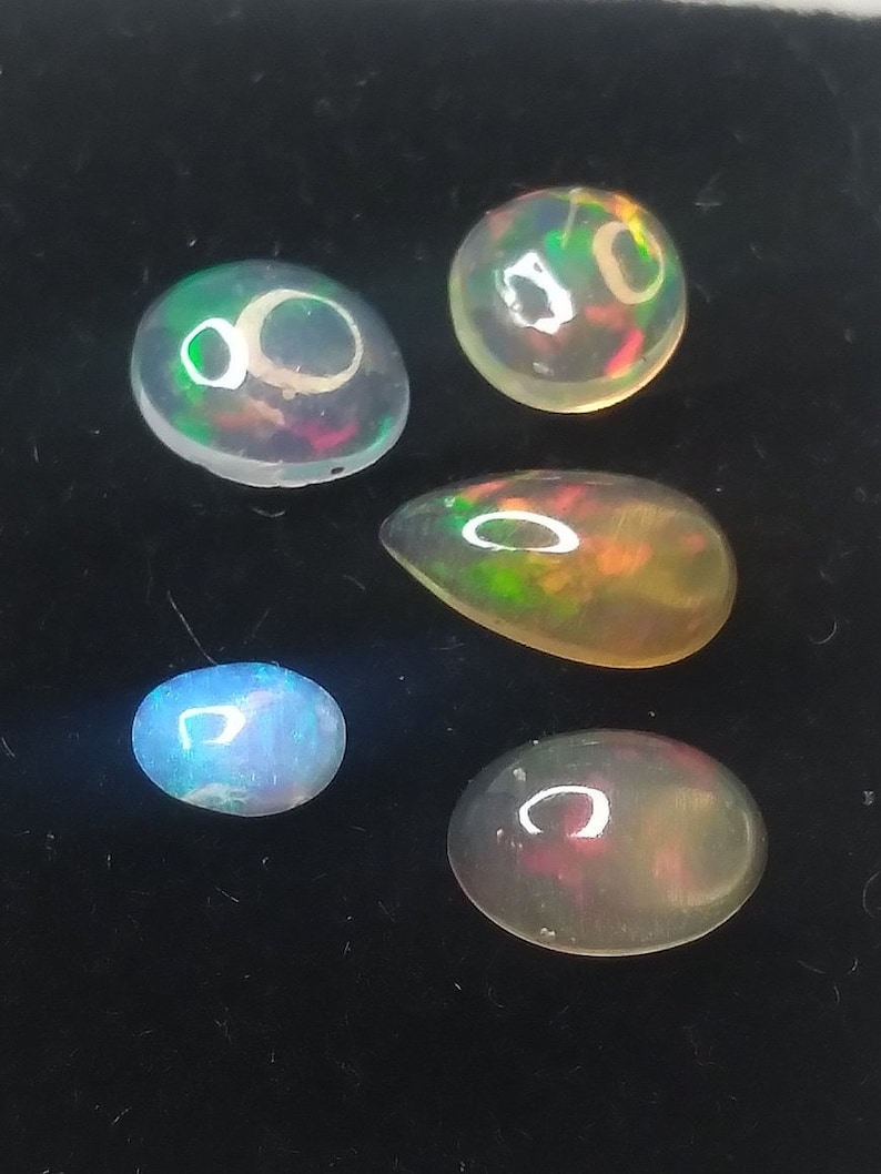May include: Five opal gemstones of various shapes and sizes, including round, oval, and teardrop, with iridescent colors of green, blue, and red.
