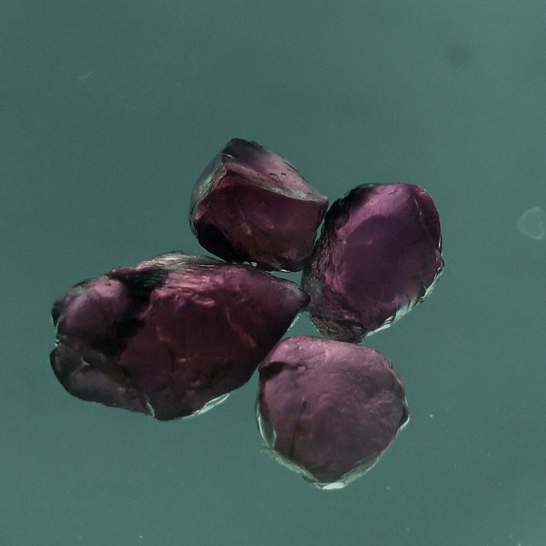May include: Four small, irregularly shaped, purple gemstones. The gemstones are translucent and have a slightly rough surface.