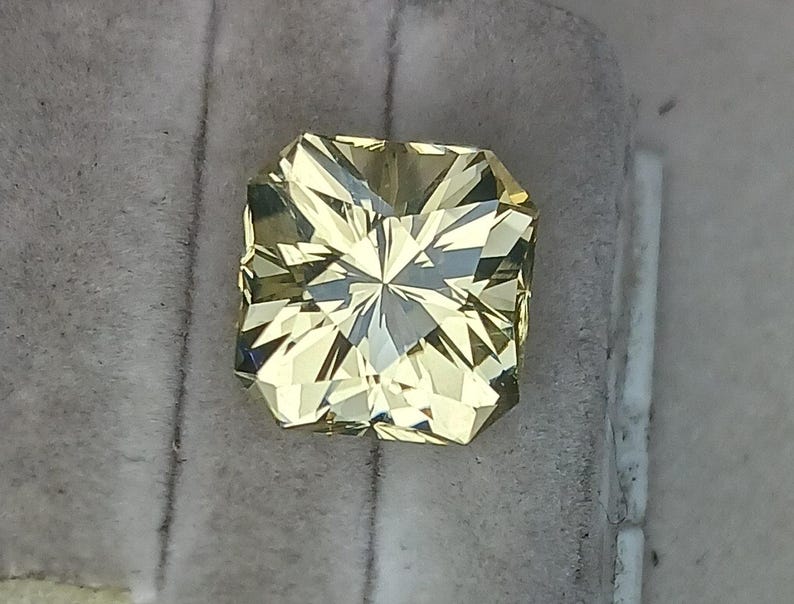 May include: A square-shaped, faceted, yellow gemstone with a star-like pattern in the centre.