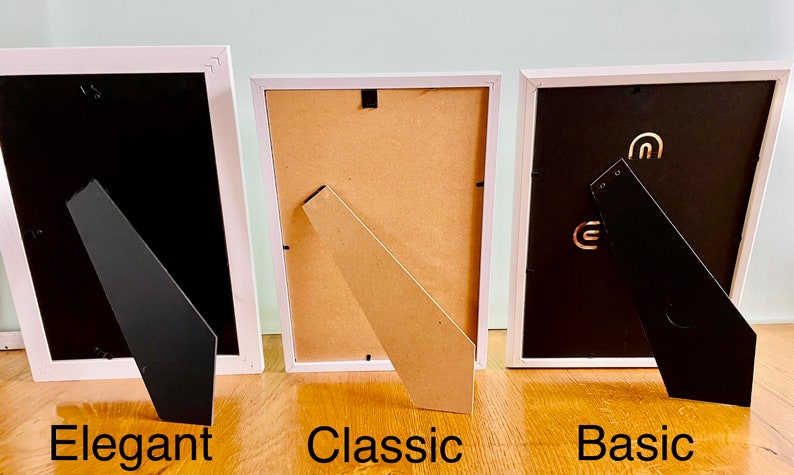 May include: Three white picture frames with different styles of easel backs. The frame on the left has a black easel back, the middle frame has a brown easel back, and the frame on the right has a black easel back. The frames are labeled "Elegant", "Classic", and "Basic" from left to right.