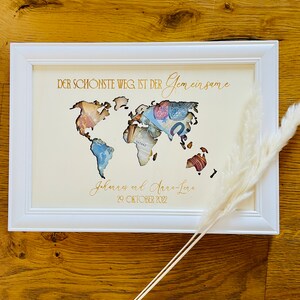 May include: A white picture frame with a gold inscription that reads "DER SCH&Ouml;NSTE WEG IST DER Gemeinsame Johannes und Anna-Lena 29. OKTOBER 2022". The frame contains a world map cutout with a background of currency bills.