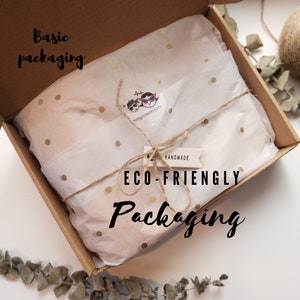 Peut inclure: Une bo&icirc;te en carton marron avec un rev&ecirc;tement en papier de soie blanc &agrave; pois dor&eacute;s. Le papier de soie est attach&eacute; avec de la ficelle et une petite &eacute;tiquette blanche qui dit "HANDMADE ECO-FRIENDLY Packaging". La bo&icirc;te est ouverte et le papier de soie est visible. Le texte "Basic packaging" est &eacute;crit sur la bo&icirc;te.