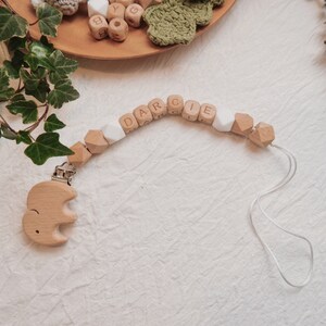 Peut inclure: Un hochet en bois pour b&eacute;b&eacute; avec le nom "DARCIE" &eacute;crit en lettres blanches. Le hochet est muni d'un &eacute;l&eacute;phant en bois attach&eacute; &agrave; un clip.