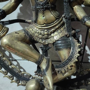 Op de afbeelding: Een gouden beeld van een hindoe&iuml;stische godheid met meerdere armen, dansend op een kleiner figuur. Het beeld is ingewikkeld versierd met sieraden en kleding.