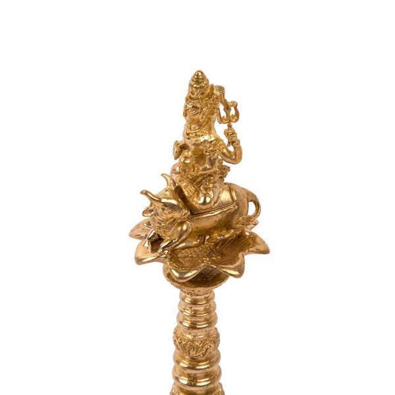 Op de afbeelding: Een gouden metalen beeld van een godheid die op een stier rijdt, staande op een lotusbloembasis. Het beeld is ingewikkeld gedetailleerd en heeft een traditioneel Indiaas ontwerp.
