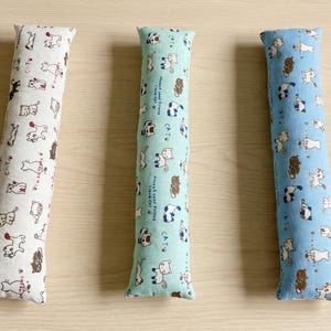 May include: Three long, rectangular fabric cat toys arranged vertically. The left toy is white, the center is light green, and the right is light blue. Each features a repeating pattern of small cartoon cats and the text CAT in black ink.