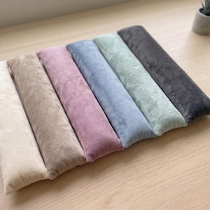 May include: A set of six rectangular, plush, velvet-textured cushions arranged side-by-side in a row. The cushions feature a soft, matte finish and come in a gradient of colors including cream, beige, dusty rose, light blue, sage green, and charcoal gray.