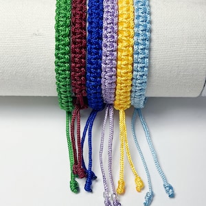 May include: Set of seven colorful friendship bracelets with tassels. The bracelets are made of braided cord in green, burgundy, blue, lavender, yellow, and light blue.