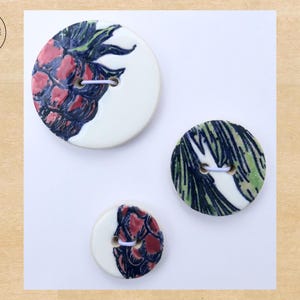 May include: Three ceramic buttons with hand-painted designs. Two buttons feature a red and dark blue floral pattern on a white background. The third button has a green and blue leaf pattern. Each button has two holes for sewing.