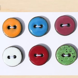 Peut inclure: Six boutons ronds colorés avec deux trous chacun. Les boutons sont dans les tons orange, bleu, bordeaux, blanc, rouge et vert avec un motif tacheté. Chaque bouton a une bordure marron foncé et du fil blanc.