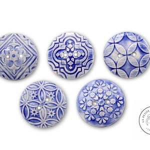 Può includere: Cinque bottoni in ceramica con motivi geometrici blu e bianchi. I bottoni sono rotondi e hanno due fori ciascuno. I bottoni sono etichettati "La Petite Boutonnerie Ceramqiues".