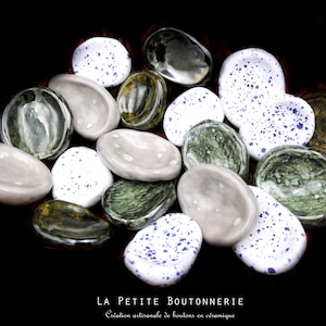 Peut inclure: Une collection de boutons en céramique de différentes couleurs et motifs, notamment vert, blanc et bleu. Les boutons ont la forme de petites pierres plates. Le texte "LA PETITE BUTTONNERIE" et "Création artisanale de boutons en céramique" est visible en bas de l'image.