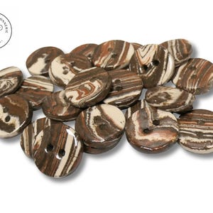 Peut inclure: Un ensemble de boutons en céramique avec un motif marbré dans des tons de marron, crème et rouille. Chaque bouton est rond avec deux trous pour la couture. Les boutons sont disposés sur un fond blanc. L'image comprend un logo en haut à gauche.