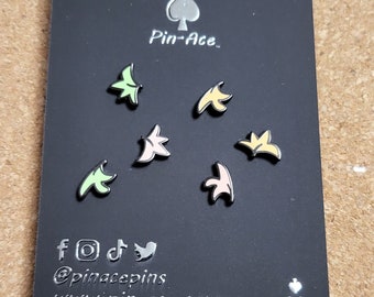 May include: A black card with a silver ace of spades and the text "Pin-Ace" in white. There are six colorful enamel pins on the card, each shaped like a stylized leaf. The pins are in shades of green, yellow, pink, and orange. The bottom of the card has the text "@pinacpinst www.pin-ace.com" in silver.