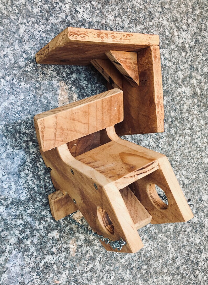Pu&ograve; includere: Un mangiatoia per uccelli in legno con una catena appesa alla parte inferiore. La mangiatoia ha una piccola apertura sul lato e un posatoio in cima. La mangiatoia &egrave; realizzata in legno naturale e ha un aspetto rustico.