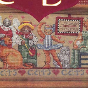 May include: Cross-stitch artwork featuring anthropomorphic cats in various costumes. One cat wears angel wings, another a farmer's outfit, and a third a ballerina's attire. The sign reads "Cat-Lovers Anonymous". The word "Cats" is repeated across the bottom.