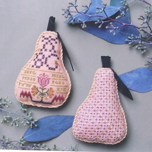 Puede incluir: Dos adornos en forma de pera con tallos negros y costuras decorativas. Uno está bordado intrincadamente con patrones florales y geométricos, el otro tiene una textura tejida. El fondo incluye hojas azules y ramitas.