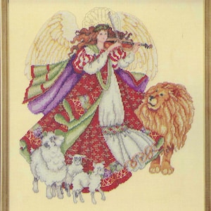 May include: Cross-stitch picture of an angel playing a violin, dressed in a red and green gown, with a lion and sheep. The angel has large white wings and long red hair. The artwork is framed in a gold-coloured wooden frame.