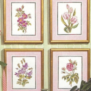 May include: Four framed floral cross-stitch artworks. Each piece features a different flower arrangement in shades of pink, purple, and green, set against a white background. The frames are gold with pink matting, creating a classic, decorative aesthetic.