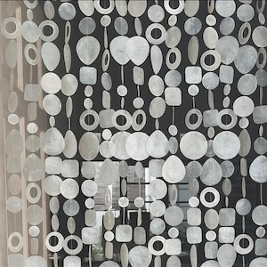 Puede incluir: Cortina decorativa hecha de numerosas piezas irregulares, blanquecinas, con forma de concha. Las piezas están ensartadas en filas verticales, creando un efecto en capas. Las formas incluyen círculos, cuadrados, óvalos y lágrimas.