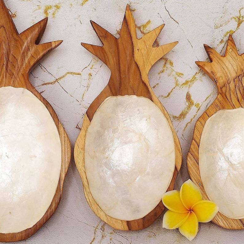 May include: Three wooden pineapple-shaped bowls with white mother-of-pearl inlays. The bowls are made of natural wood and have a rustic, handcrafted look.