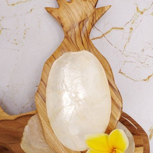 May include: A wooden pineapple shaped dish with a white mother of pearl bowl inside. A yellow flower is sitting on the dish.