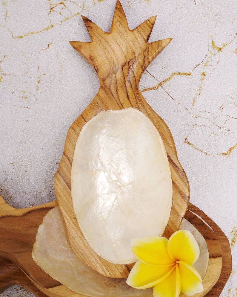 May include: A wooden pineapple shaped dish with a white mother of pearl bowl inside. A yellow flower is sitting on the dish.
