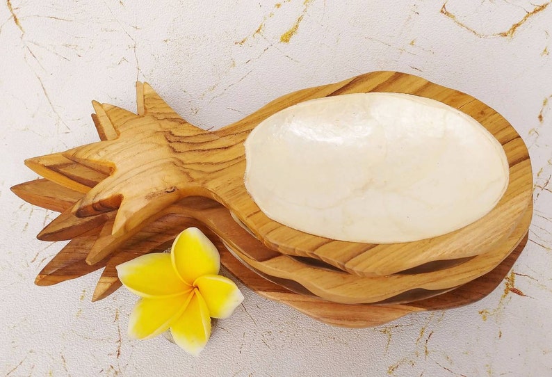 May include: A wooden pineapple shaped serving bowl with a white mother of pearl insert. The bowl is made of natural wood and has a rustic look.