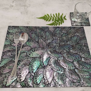 May include: A black and iridescent placemat with a pattern of overlapping butterfly wings. A fork and spoon are placed on the placemat.