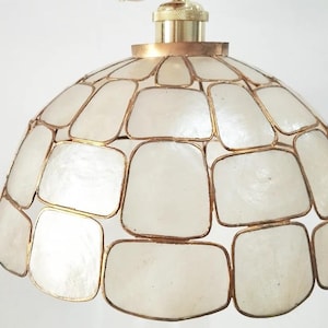 Könnte beinhalten: Ein weißer, kuppelförmiger Lampenschirm mit einem goldenen Metallrahmen. Der Lampenschirm besteht aus kleinen, quadratischen Teilen aus Perlmutt.