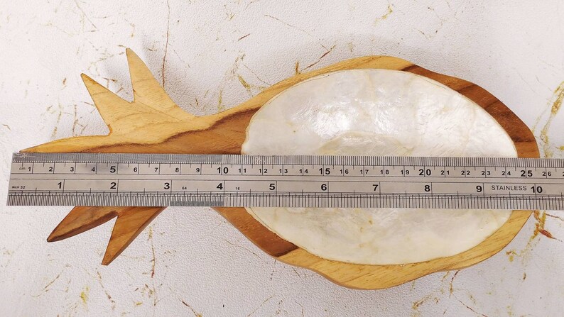 May include: A wooden pineapple-shaped dish with a white mother-of-pearl inlay. The dish is approximately 9 inches long.