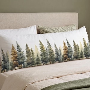 May include: A long, rectangular body pillow with a watercolor forest design. The pillow features a row of evergreen trees in shades of green, brown, and yellow against a white background. The pillow is on a bed with white sheets.
