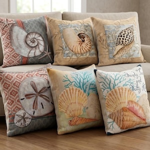 Puede incluir: Un conjunto de cojines decorativos con diseños marinos. Los cojines presentan ilustraciones de conchas marinas, estrellas de mar y dólares de arena en tonos beige, azul y coral. Algunos cojines tienen el texto "Sandy Toes and Salty Kisses."