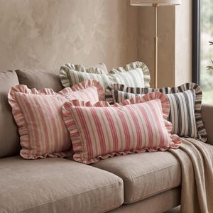 May include: Three rectangular throw pillows with ruffled edges arranged on a sofa. One pillow features pink and cream vertical stripes, another has green and cream stripes, and the third displays black and cream stripes, all with matching fabric ruffles.