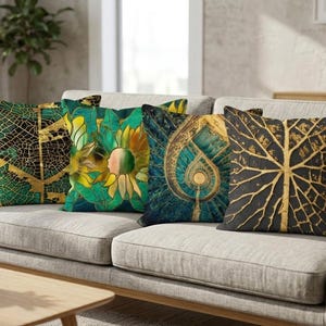 May include: Four decorative throw pillows with nature-inspired designs rest on a gray sofa. The pillows feature gold and green leaf and floral patterns. One pillow has a black background with a gold leaf design. The pillows add a touch of nature to home decor.