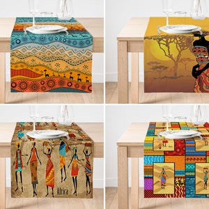 Könnte beinhalten: Vier dekorative Tischläufer mit afrikanisch inspirierten Designs. Einer zeigt eine blaue, orange und rote Landschaft mit Giraffen. Ein anderer zeigt die Silhouette einer Frau vor einem Sonnenuntergang. Der dritte hat Figuren, die Körbe tragen, und der letzte ist ein Patchwork-Design.