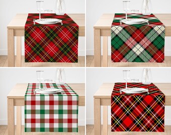 May include: A collection of four rectangular table runners featuring various plaid and checkered patterns in red, green, white, and black. Each runner is displayed on a wooden table with a white plate, a glass, and a fork placed on top.