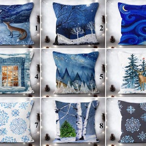 Könnte beinhalten: Neun verschiedene Kissen-Designs mit Winterszenen. Die Kissen sind alle quadratisch und haben einen weißen Hintergrund mit blauen und weißen Designs. Die Designs beinhalten einen Fuchs, ein Fenster, eine Bergkette, ein Reh, ein Schneeflockenmuster und einen Birkenwald.