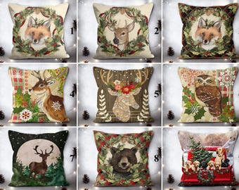 May include: A collection of nine decorative cushions with festive winter designs. The cushions display images of a fox, deer, owl, bear, and puppies. Each cushion has a unique design, including wreaths, snowflakes, and a red truck.
