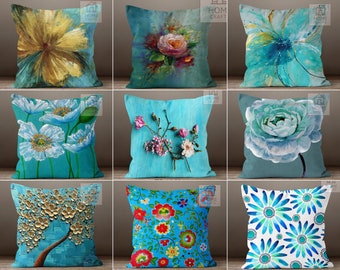 Könnte beinhalten: Eine Sammlung dekorativer Kissen mit floralen Designs. Die Kissen zeigen verschiedene künstlerische Darstellungen von Blumen in Blau-, Gelb-, Rosa- und Weißtönen. Einige Designs umfassen gemalte Blumen, andere haben strukturierte, dreidimensionale Elemente.